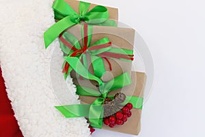 Gifts wrapped in craft paper and decorated with green and red ribbons flat lay on white background