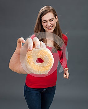 Giggling young woman grabbing a donut as junk food temptation
