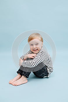 Giggly little blond boy sitting on the floor, hugging his knees. Over blue