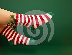Gils feet in fluffy New Year warm socks. Christmas tree branch with balls decorats female leg