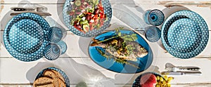 Gilt-head bream also known as Orata baked in the oven and served on a white wooden table with vegetable salad and fruits. Healthy