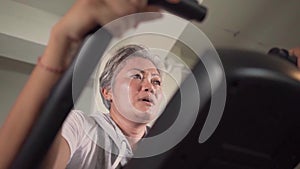 Gimbal static bicycle shot on middle aged attractive and sweaty Asian Indonesian woman with grey hair training sweating at gym