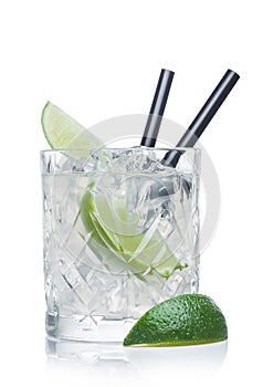 Gimlet cocktail in crystal glass with ice cubes and straw and lime slices on white