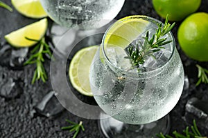 Gin and Tonic Alcohol drink with Lime, Rosemary and ice on rustic black table