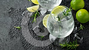 Gin and Tonic Alcohol drink with Lime, Rosemary and ice on rustic black table