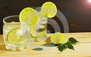 Gin and tonic cocktail with lime pieces and ice cubes in two glasses side view