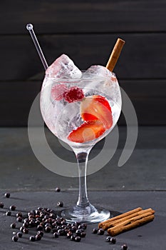 Gin tonic cocktail with strawberries cinnamon and juniper