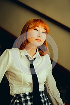 A ginger Asian schoolgirl in a black tie stands on the school staircase. Education, youth, and personal expression through the