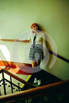 A ginger Asian schoolgirl stands on the school staircase on a sunny day.