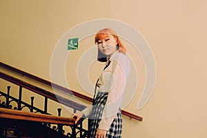 A ginger Asian student in uniform, standing on a staircase with a smile on her face. Diversity, and youth. It represents the