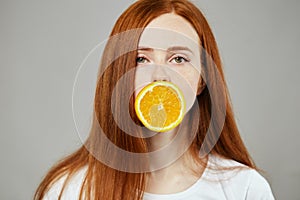 Ginger attractive girl covering her mouth with a slice of orange