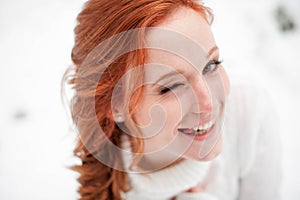 Ginger attractive girl in white sweater in winter forest. Snow december in park. Portrait. Christmas cute time.