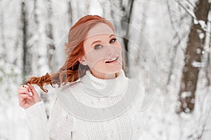 Ginger beautiful girl in white sweater in winter forest. Snow december in park. Christmas time.
