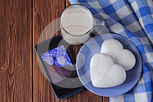 ginger biscuits in the shape of heart on a saucer, a cup of hot chocolate and smarfon on a wooden table