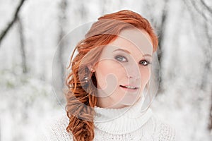 Ginger caucasian girl in white sweater in winter forest. Snow december in park. Portrait. Christmas cute time.