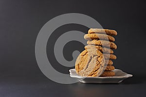 A ginger cookie leans on a stack of cookies on a white plate with a black background