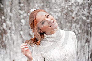 Ginger cute girl in white sweater in winter forest. Snow december in park. Christmas time.