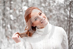 Ginger european girl in white sweater in winter forest. Snow december in park. Christmas magic time.