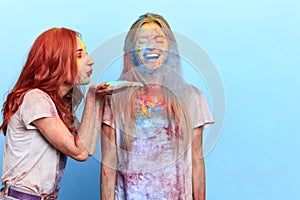 Ginger girl blowing colored powder to her friend`s face