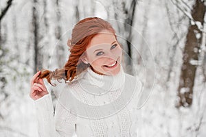 Ginger girl in white sweater in winter forest. Snow december in park. Christmas time.