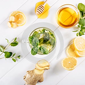 Ginger green tea in a glass for flu cold winter days. Side view on white wooden background decorated with mint, lemon