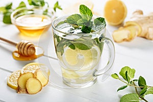 Ginger green tea in a glass for flu cold winter days. Side view on white wooden background decorated with mint, lemon