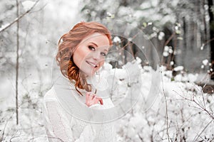 Ginger happy girl in white sweater in winter forest. Snow december in park. Portrait. Christmas cute time.