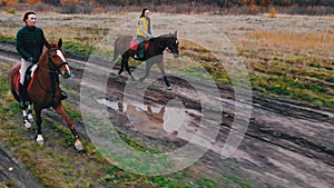 Ginger horses with equestrians on their back are galloping on the road with puddles