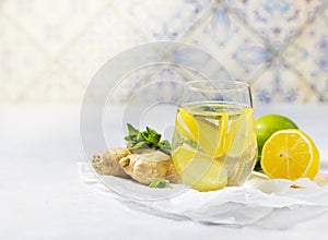 Ginger-lemon drink. Homemade Organic ginger in a glass with Lemon and mint on white table. Trendy detox healthy drink