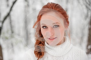 Ginger nice girl in white sweater in winter forest. Snow december in park. Portrait. Christmas cute time.