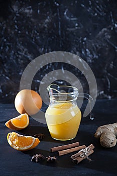 Ginger-orange juice in a glass pitchers, oranges, ginger and cinnamon on a black background. Copy spaes. Healthy eating