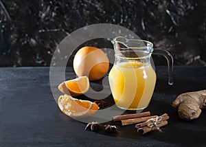 Ginger-orange juice in a glass pitchers, oranges, ginger and cinnamon on a black background. Fresh drink. Healthy eating