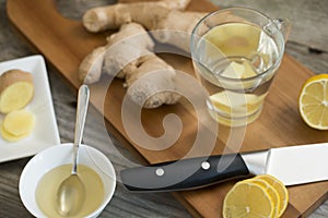 Ginger root, lemon, hot water and honey on wooden cutting board, healthy ingredients for tea against cold