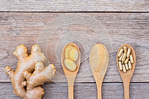 Ginger root and slices, dried ginger powder and powder capsules in wooden spoon isolated on wood table background.