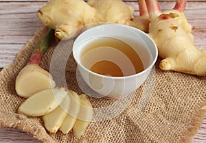 Ginger root and slices on wood background with cup of ginger tea. healthy drink.