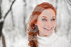 Ginger smiling girl in white sweater in winter forest. Snow december in park. Portrait. Christmas cute time.