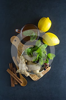 Ginger tea cup with lemons and mint leaves on dark background. Ginger tea, drink ingredients, cold and autumn time