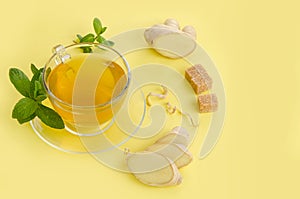 Ginger tea with lemon in glass Cup with brown organic sugar and mint on yellow paper background