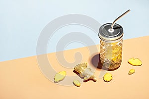 Ginger water in stylish jar with metal straw on geometric paper background and ginger slices, isometric view