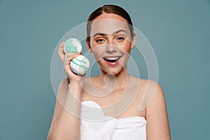 Ginger woman wearing towel smiling while showing balls bath bomb