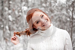 Ginger young girl in white sweater in winter forest. Snow december in park. Christmas time.