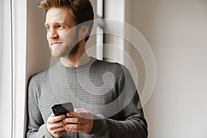 Ginger young man using mobile phone while leaning on wall