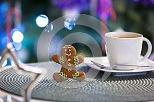 Gingerbread cookie man at the cup of hot coffee and christmas tree lights in background