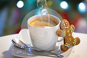 Gingerbread cookie man at the cup of hot coffee and christmas tree lights in background