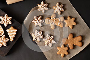 Gingerbread cookie with and without sugar icing on parchment and black table background. Snowflake, man, Christmas tree