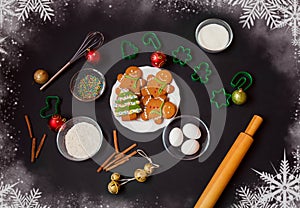 Gingerbread cookies, cookie cutters, kitchen utensils, ingredients for baking and christmas decorations on dark background.