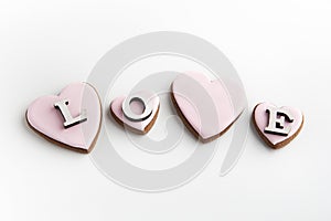 Gingerbread cookies in heart-shaped with pink sugar icing on white background and inscription LOVE