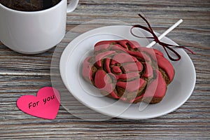 Gingerbread in the form of a flower of a red rose , paper in the form of heart with an inscription and a cup with coffee