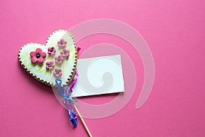 Gingerbread heart with white icing and pink flowers shit of paper on pink background. Love concept. Gift for womans and valentines