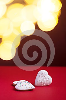 Gingerbread hearts with white icing and white and colorful sprinkles on red background with fairy lights